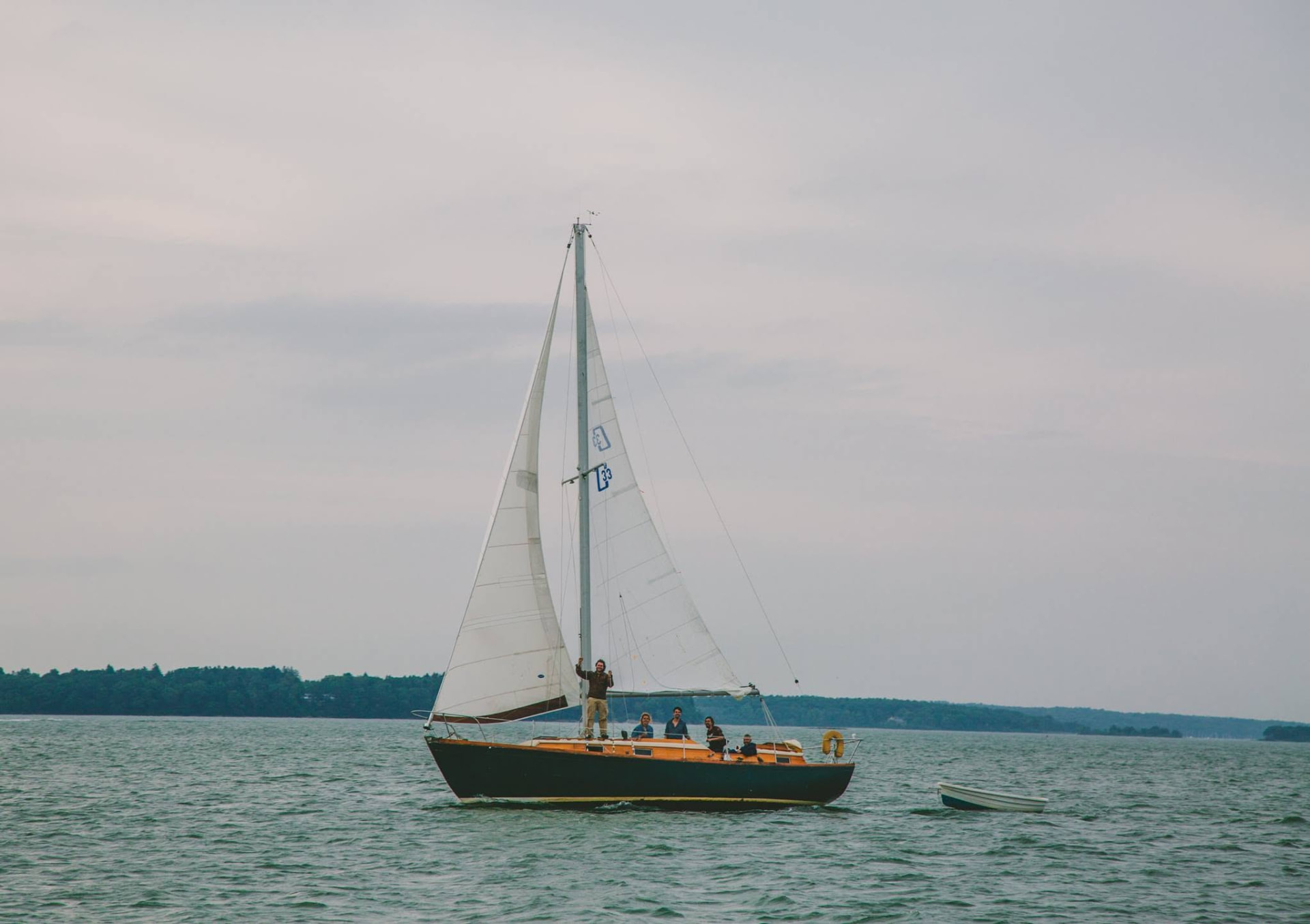A small sailboat with people aboard under grey skies on Casco Bay